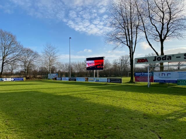 LED-Anzeigetafel auf einem Mast am Rand eines Fußballplatzes
