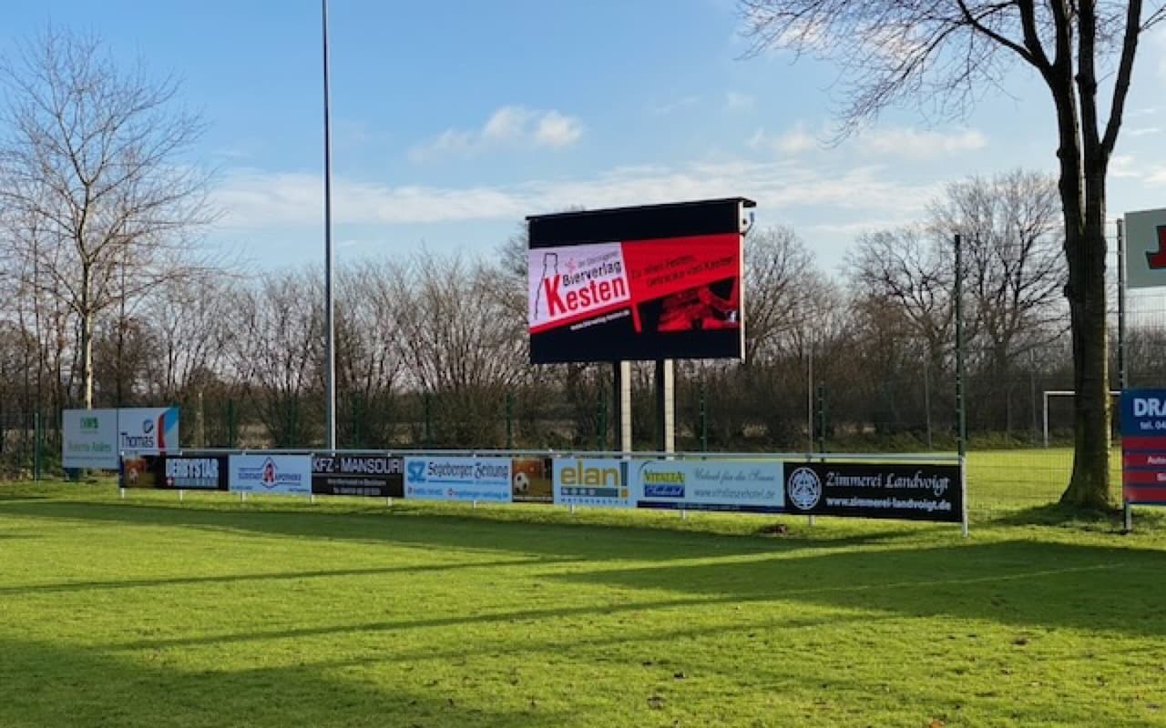 LED-Anzeigetafel am Sportplatz bei Sonnenschein mit Werbemotiv