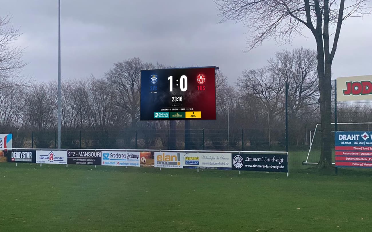 LED-Anzeigetafel auf einem Pylon hinter einem Sportplatz mit Spielstand