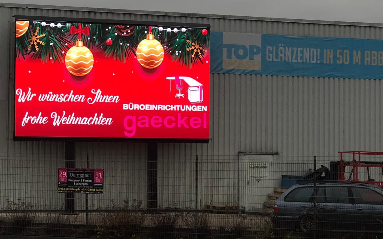 LED-Wand auf zwei Stützen mit Weihnachtsmotiv vor einer Gewerbehalle