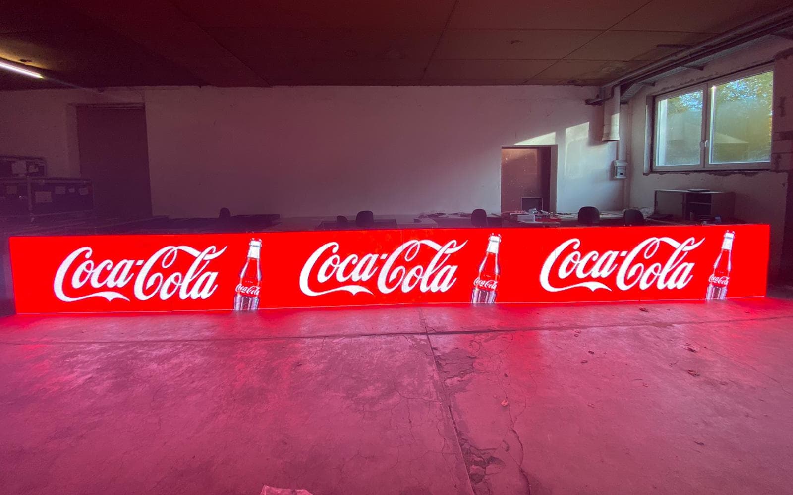 LED-Bande mit roter Coca-Cola-Werbung vor Tischen in einer Lagerhalle