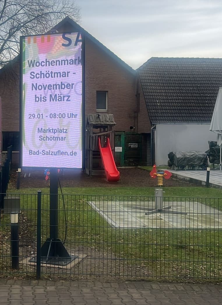 LED-Stele mit Kundenwerbung auf einem Einzelmast neben einem Gehweg